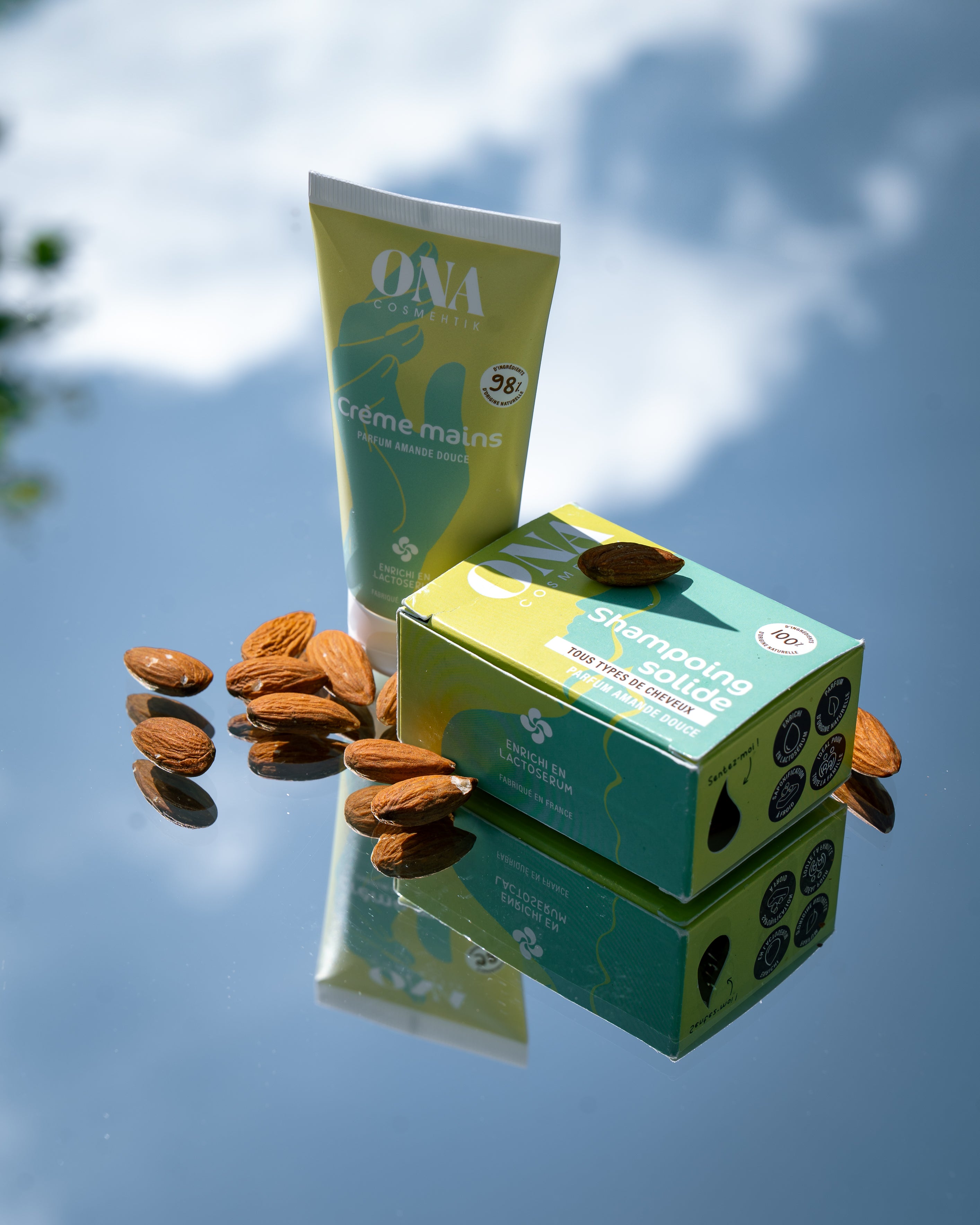Un tube de crème mains et un shampoing solide de la marque ONA COSMEHTIK entourés d'amandes. 