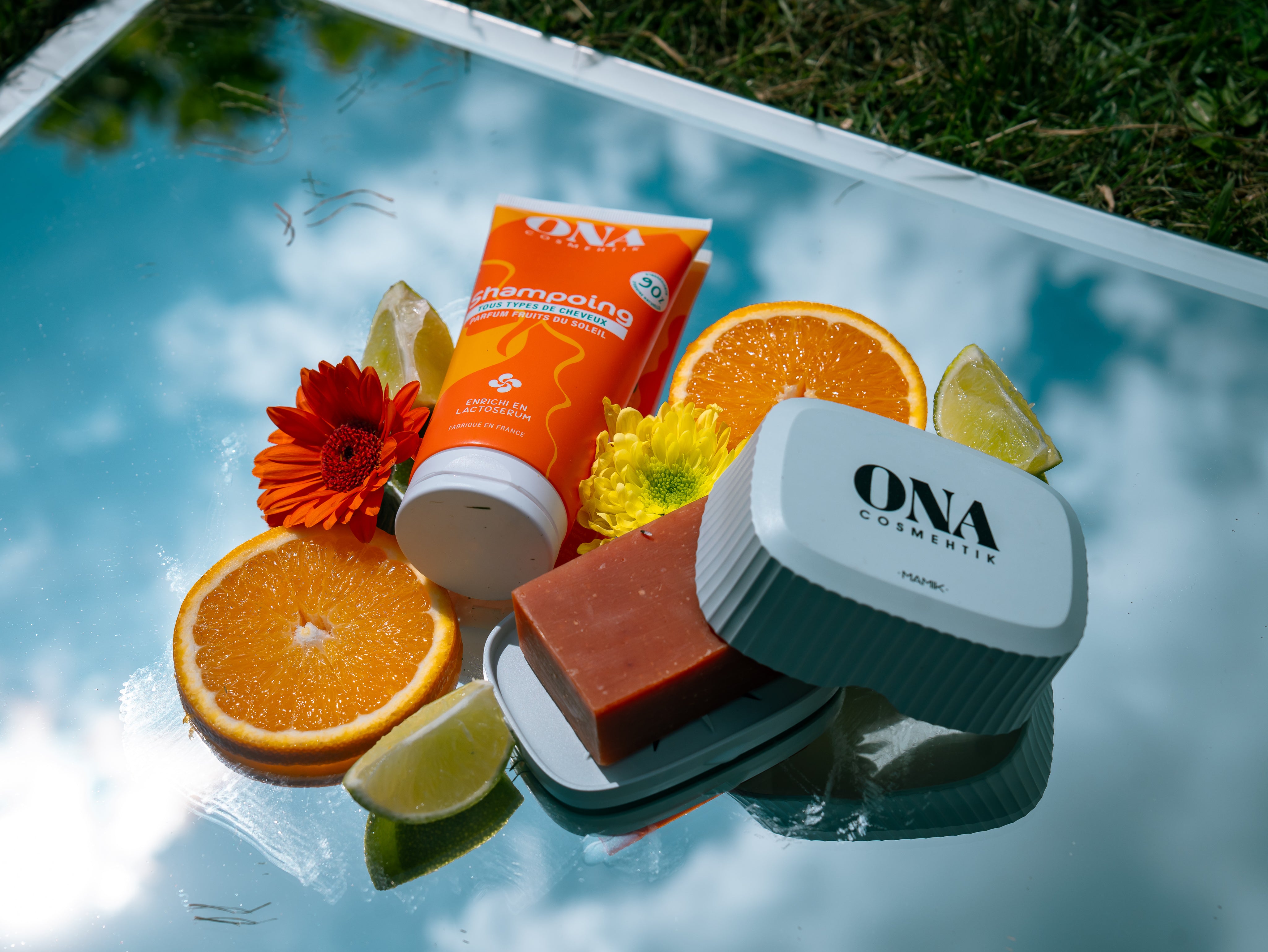 Composition de produits cosmétiques entourés d'agrumes et de fleurs oranges et jaunes.